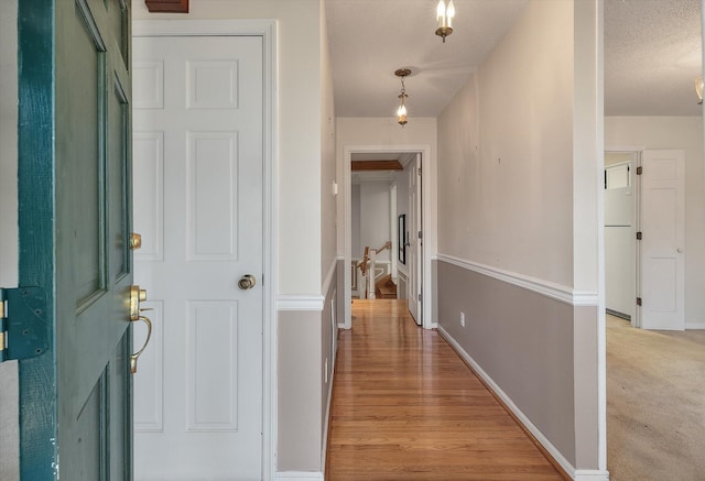 hall featuring a textured ceiling, baseboards, light colored carpet, and light wood finished floors