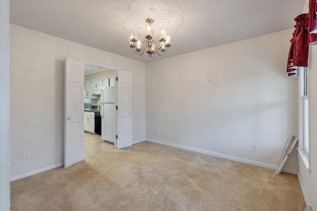 empty room with a textured ceiling, baseboards, a chandelier, and light carpet