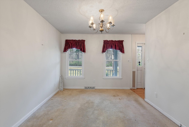 spare room featuring visible vents, a textured ceiling, carpet, an inviting chandelier, and baseboards