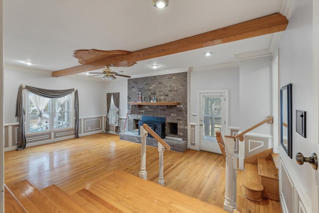 living room featuring beam ceiling, a brick fireplace, light wood-style flooring, and a decorative wall