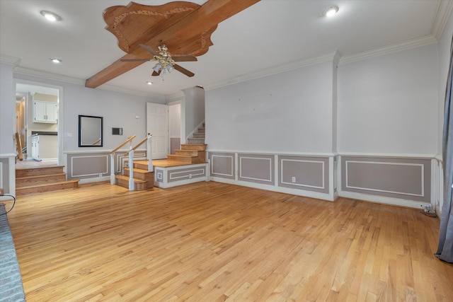 unfurnished living room with light wood finished floors, crown molding, ceiling fan, stairs, and a decorative wall