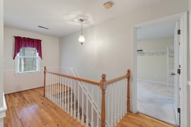 hall with wood finished floors, an upstairs landing, visible vents, and a textured ceiling