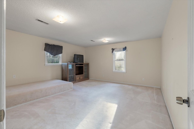 unfurnished living room featuring light colored carpet, visible vents, and a textured ceiling