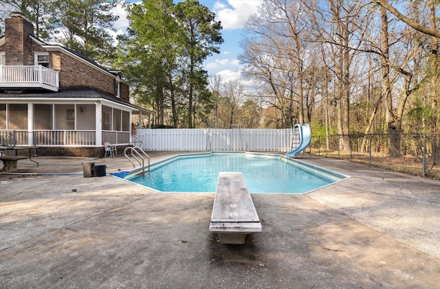 view of pool featuring a water slide, fence, a sunroom, a patio, and a diving board