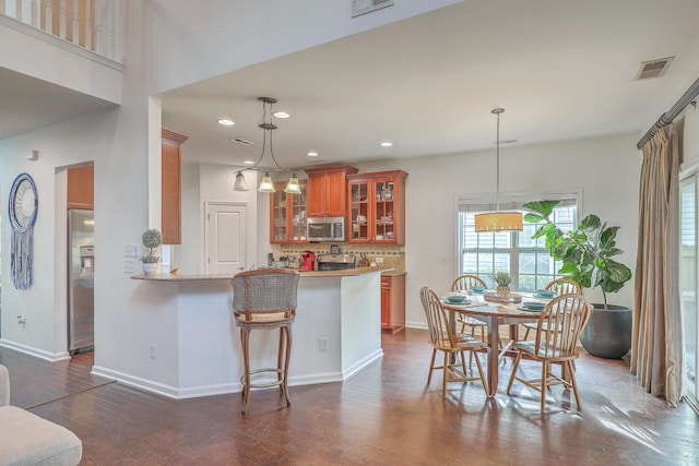 kitchen featuring brown cabinetry, visible vents, a peninsula, stainless steel appliances, and decorative backsplash