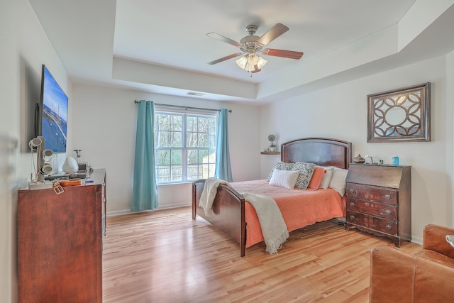 bedroom featuring a tray ceiling, light wood-style floors, visible vents, and baseboards