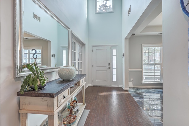 foyer featuring dark wood finished floors, visible vents, plenty of natural light, and a towering ceiling