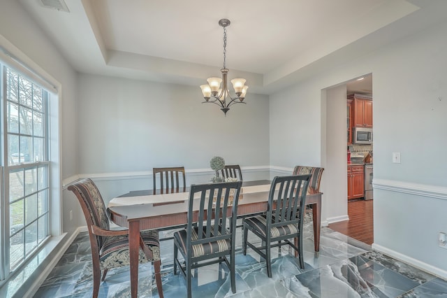 dining space featuring visible vents, a raised ceiling, a notable chandelier, and baseboards