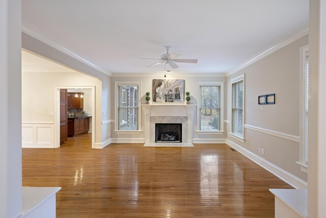 unfurnished living room with ceiling fan, light hardwood / wood-style floors, ornamental molding, and a high end fireplace