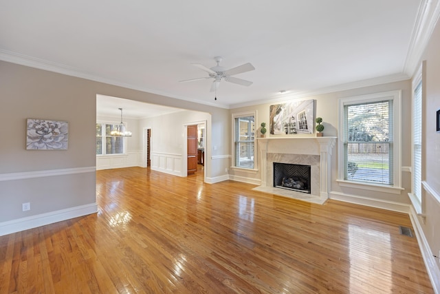 unfurnished living room with a high end fireplace, wood-type flooring, ceiling fan with notable chandelier, and ornamental molding