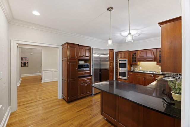 kitchen featuring kitchen peninsula, premium range hood, built in appliances, decorative light fixtures, and light hardwood / wood-style flooring