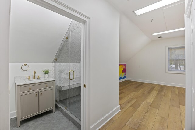 bathroom with vaulted ceiling with skylight, vanity, a shower with door, and hardwood / wood-style floors