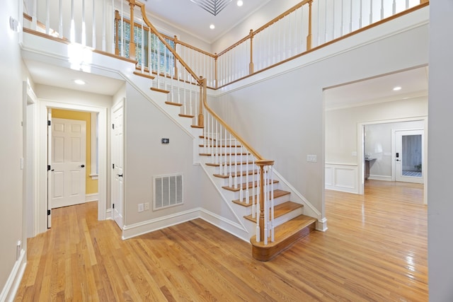 stairs with a high ceiling, crown molding, and hardwood / wood-style floors