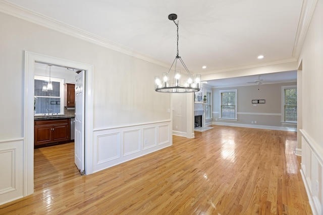 unfurnished dining area featuring ceiling fan with notable chandelier, light hardwood / wood-style flooring, and crown molding