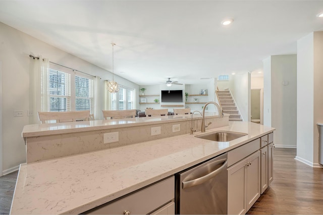 kitchen featuring light stone countertops, a sink, dark wood-type flooring, stainless steel dishwasher, and decorative light fixtures