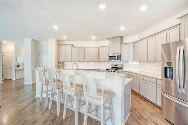 kitchen with a kitchen island with sink, gray cabinetry, decorative backsplash, stainless steel appliances, and light wood-type flooring