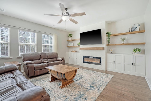 living area featuring visible vents, ceiling fan, a fireplace, and light wood-style floors