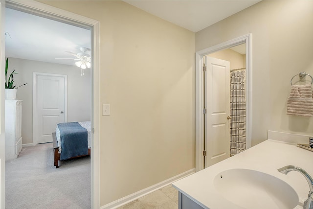 ensuite bathroom featuring a ceiling fan, baseboards, double vanity, a sink, and ensuite bathroom