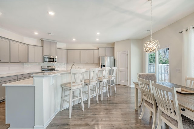 kitchen with wood finished floors, gray cabinets, a large island with sink, stainless steel appliances, and decorative backsplash