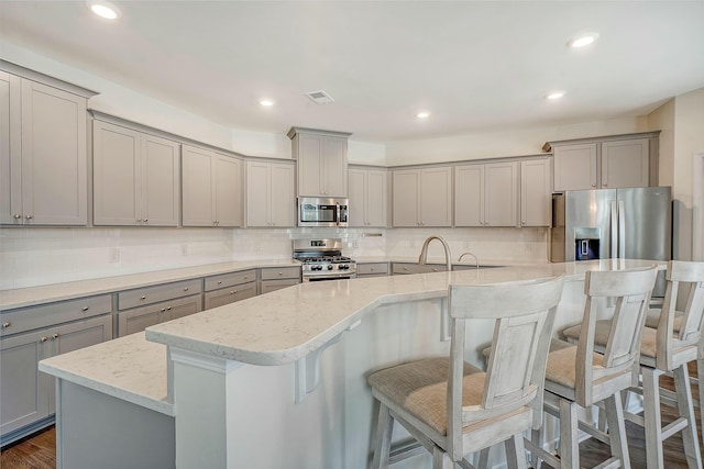 kitchen with visible vents, gray cabinetry, light stone countertops, an island with sink, and stainless steel appliances