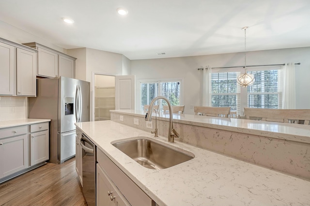 kitchen with gray cabinetry, decorative backsplash, stainless steel appliances, a sink, and decorative light fixtures