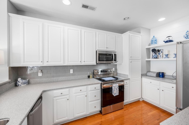 kitchen featuring light wood finished floors, visible vents, decorative backsplash, appliances with stainless steel finishes, and white cabinetry