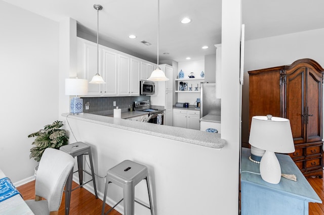 kitchen featuring a peninsula, white cabinetry, appliances with stainless steel finishes, and decorative light fixtures