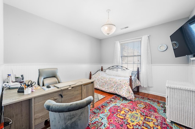 bedroom featuring a wainscoted wall, visible vents, and dark wood-type flooring