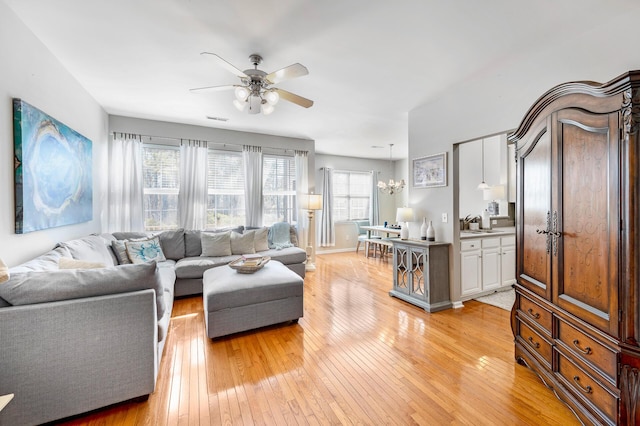 living room featuring visible vents, light wood-style flooring, baseboards, and ceiling fan with notable chandelier