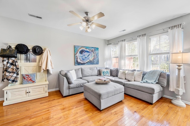 living area featuring light wood-style flooring, a ceiling fan, visible vents, and baseboards