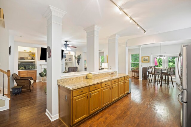 kitchen featuring dark hardwood / wood-style flooring, light stone countertops, decorative columns, and stainless steel refrigerator