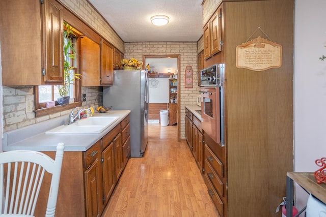 kitchen with sink, stainless steel fridge, light hardwood / wood-style floors, brick wall, and oven