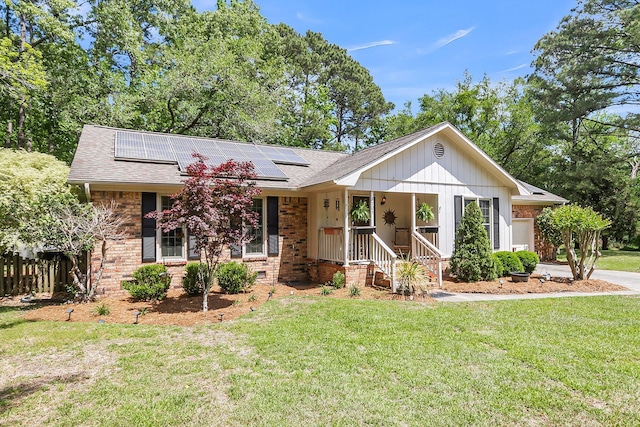 ranch-style home with brick siding, a shingled roof, a front yard, and solar panels