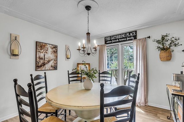 dining room with light wood-type flooring, a textured ceiling, baseboards, and an inviting chandelier
