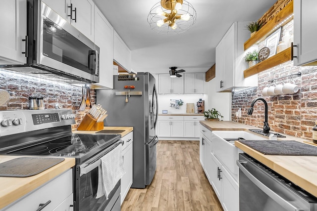 kitchen featuring a sink, butcher block counters, light wood-style floors, a ceiling fan, and stainless steel appliances