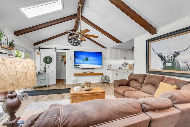 living area with beamed ceiling, a skylight, a barn door, and wood finished floors