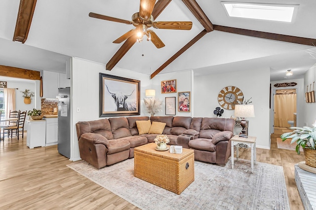 living area with ceiling fan, a skylight, light wood-type flooring, beam ceiling, and high vaulted ceiling