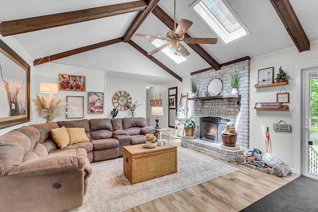 living area with a ceiling fan, lofted ceiling with skylight, wood finished floors, and a fireplace