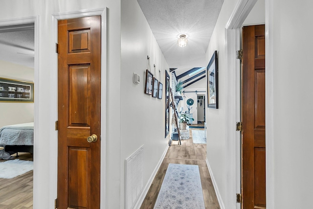 hallway featuring baseboards, a textured ceiling, wood finished floors, and visible vents