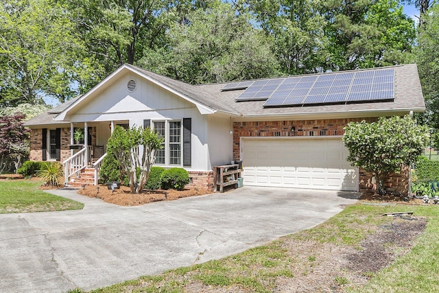 ranch-style home with a porch, solar panels, brick siding, concrete driveway, and a shingled roof