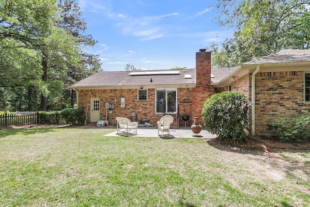 rear view of house featuring fence, a chimney, a yard, and a patio area