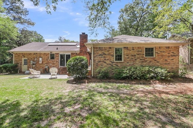 rear view of house featuring a chimney, brick siding, a patio area, entry steps, and a lawn