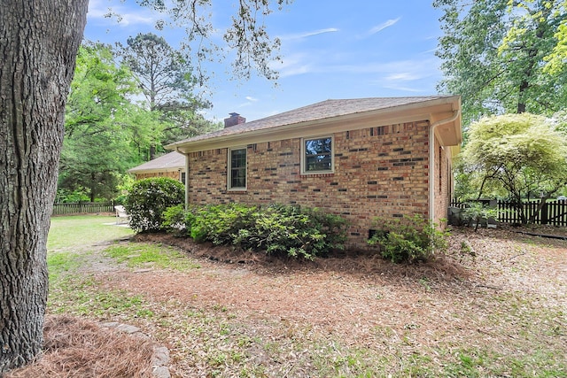 view of side of property featuring brick siding, fence, and a chimney