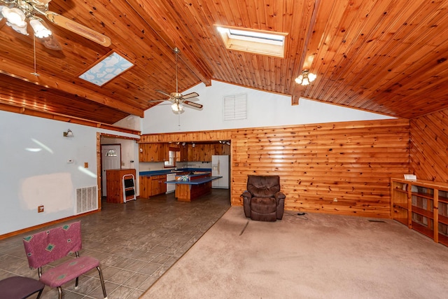 unfurnished living room with lofted ceiling with skylight, wooden ceiling, dark colored carpet, wooden walls, and ceiling fan