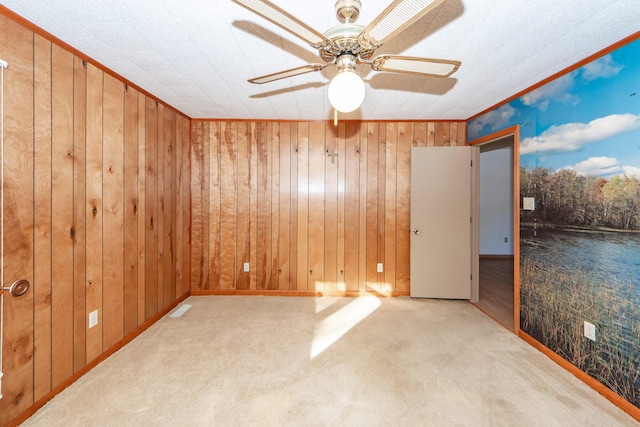 unfurnished room with ceiling fan, light colored carpet, wood walls, and ornamental molding