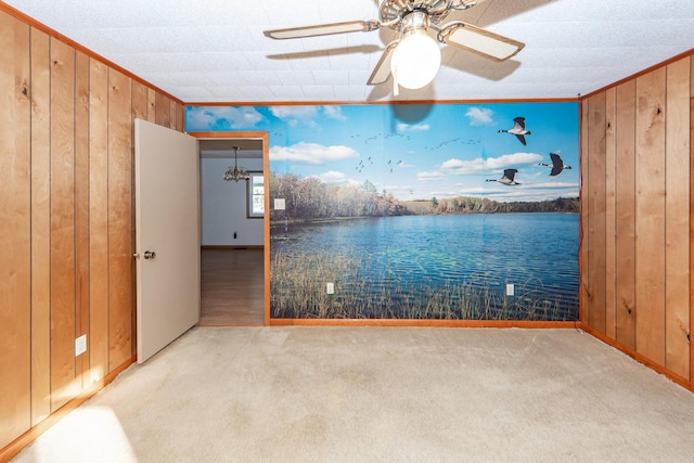 carpeted empty room with ceiling fan, crown molding, and wood walls