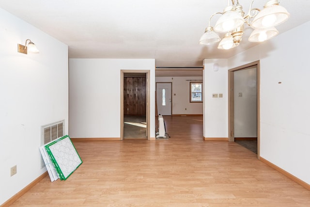 spare room with a chandelier and light wood-type flooring