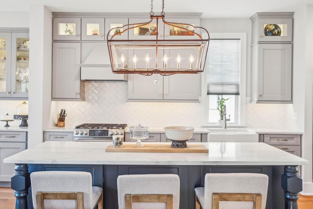 kitchen featuring a kitchen breakfast bar, stainless steel stove, gray cabinetry, and tasteful backsplash