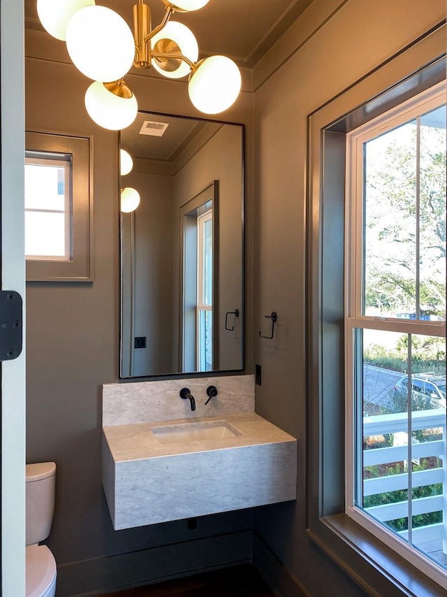 half bathroom with visible vents, an inviting chandelier, ornamental molding, toilet, and a sink