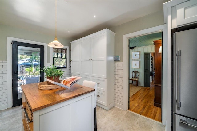 kitchen with wood counters, white cabinetry, high end fridge, and decorative light fixtures